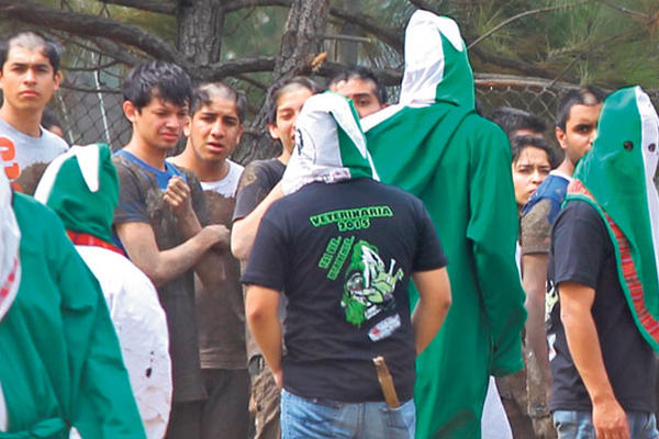 Encapuchados vigilan, a estudiantes de nuevo ingreso, a quienes les cortaron el pelo, en un "bautizo", ayer.