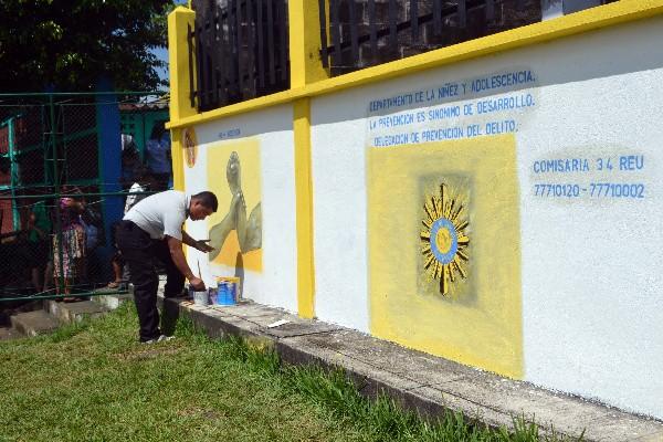 Agente pinta  mural en pared de escuela.