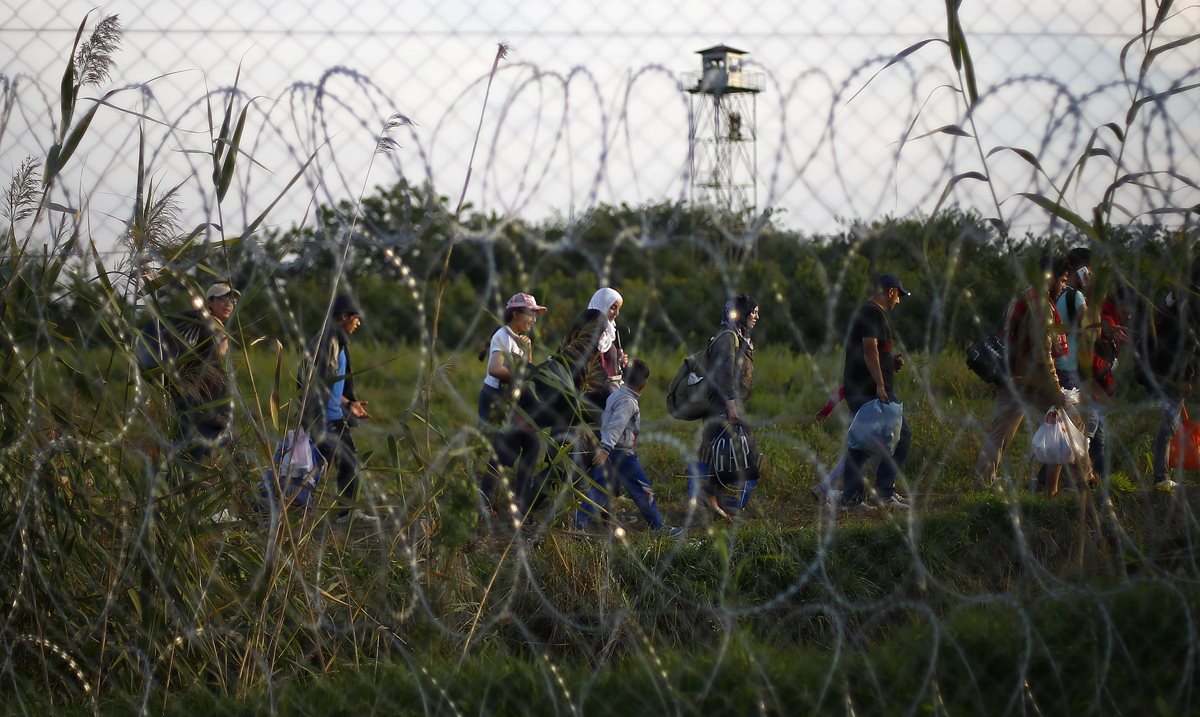 Migrantes caminan detrás de una malla que colocaron las autoridades húngaras para impedir el paso de más solicitantes de refugio. (Foto Prensa Libre: AP).