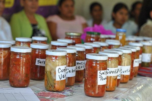 Mujeres muestran   alimentos   que han aprendido   a preparar  y  envasar.