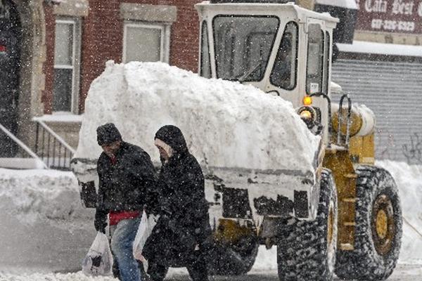 Dos personas caminan delante de una máquina quitanieves en Boston, Massachusetts, Estados Unidos. (Foto Prensa Libre: EFE)