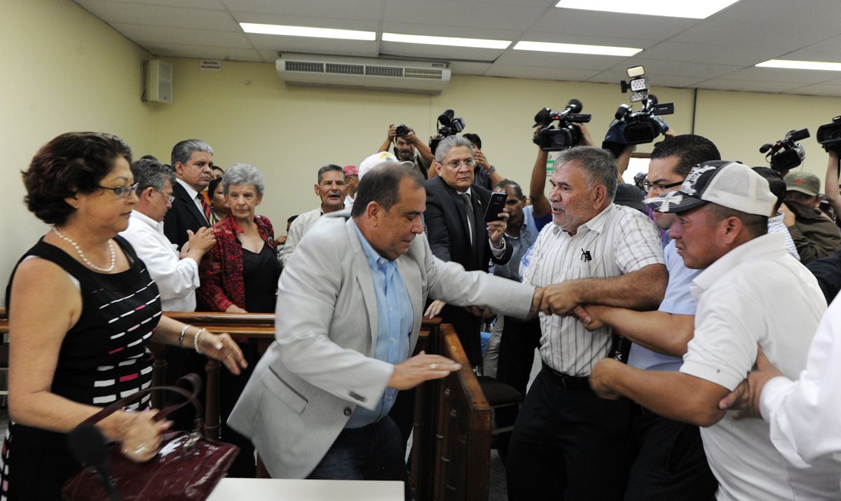 Simpatizantes y miembros del partido Libre toman al periodista David Romero (centro, de camisa celeste), para llevarlo hacia un lugar fuera de los tribunales. (Foto Prensa Libre: AFP).