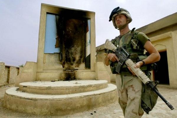 Un soldado de EE. UU. camina frente a un retrato quemado de Sadam Hussein, en An Nasiriyah, Irak?. (Foto Prensa Libre: AFP).