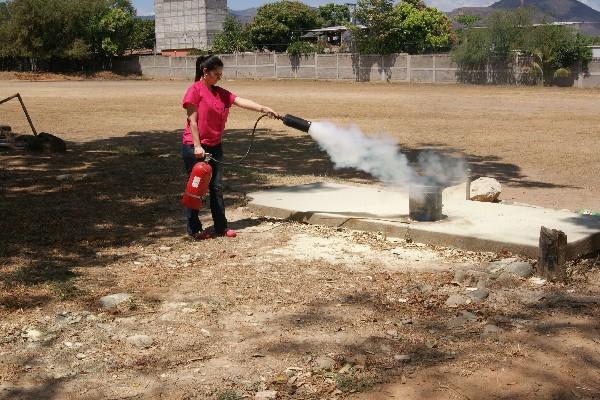 Una empleada practica el uso de un extinguidor  en un campo ubicado a una costado del hospital.