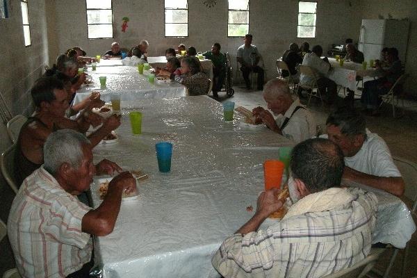 Personas de la tercera edad platican mientras degustan un sencillo desayuno, en Los Amates.