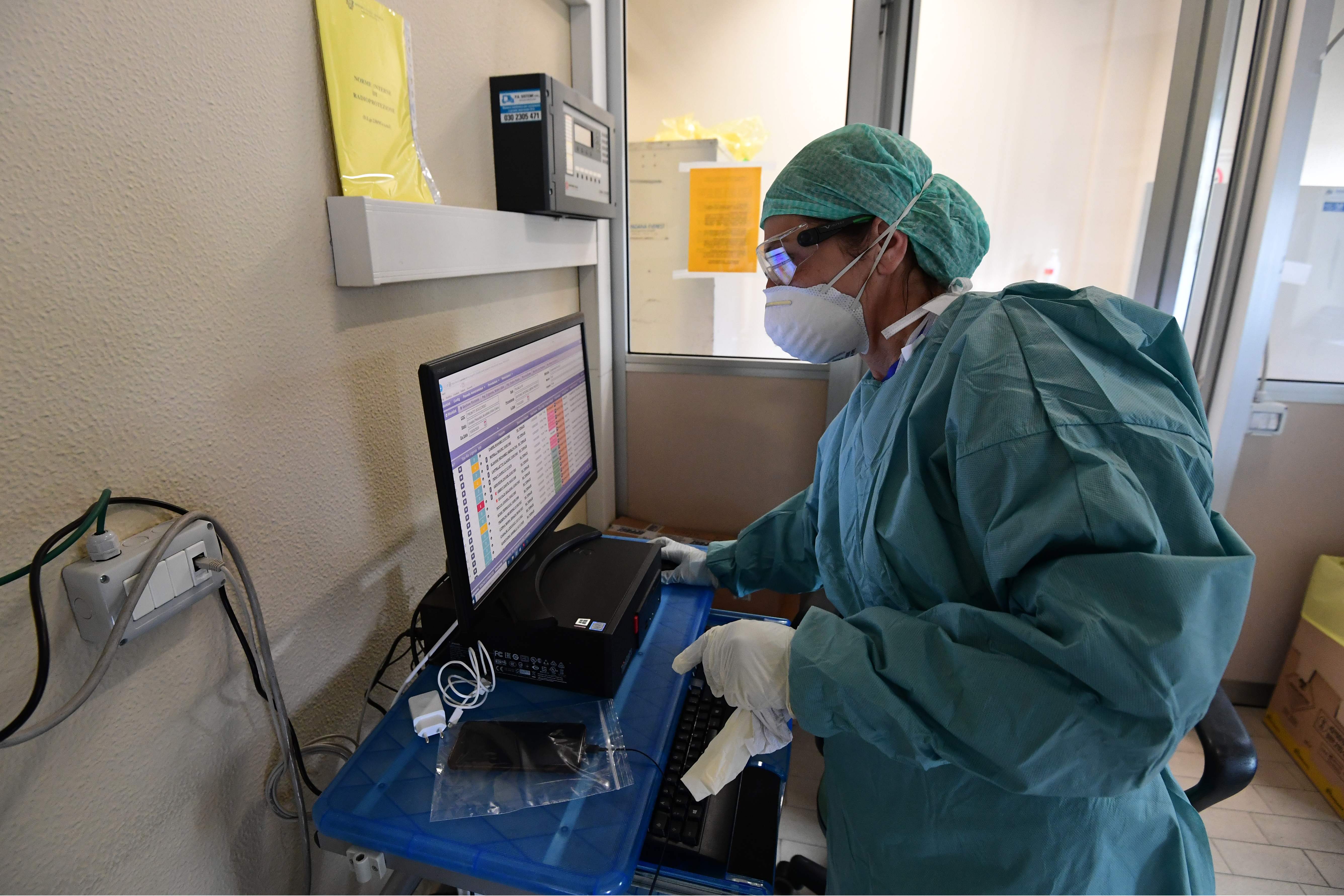 A hospital worker wearing protective mask and gear works in the radiology section at a temporary emergency structure set up outside the accident and emergency department, where any new arrivals presenting suspect new coronavirus symptoms are being tested, at the Brescia hospital, Lombardy, on March 13, 2020. (Photo by Miguel MEDINA / AFP)