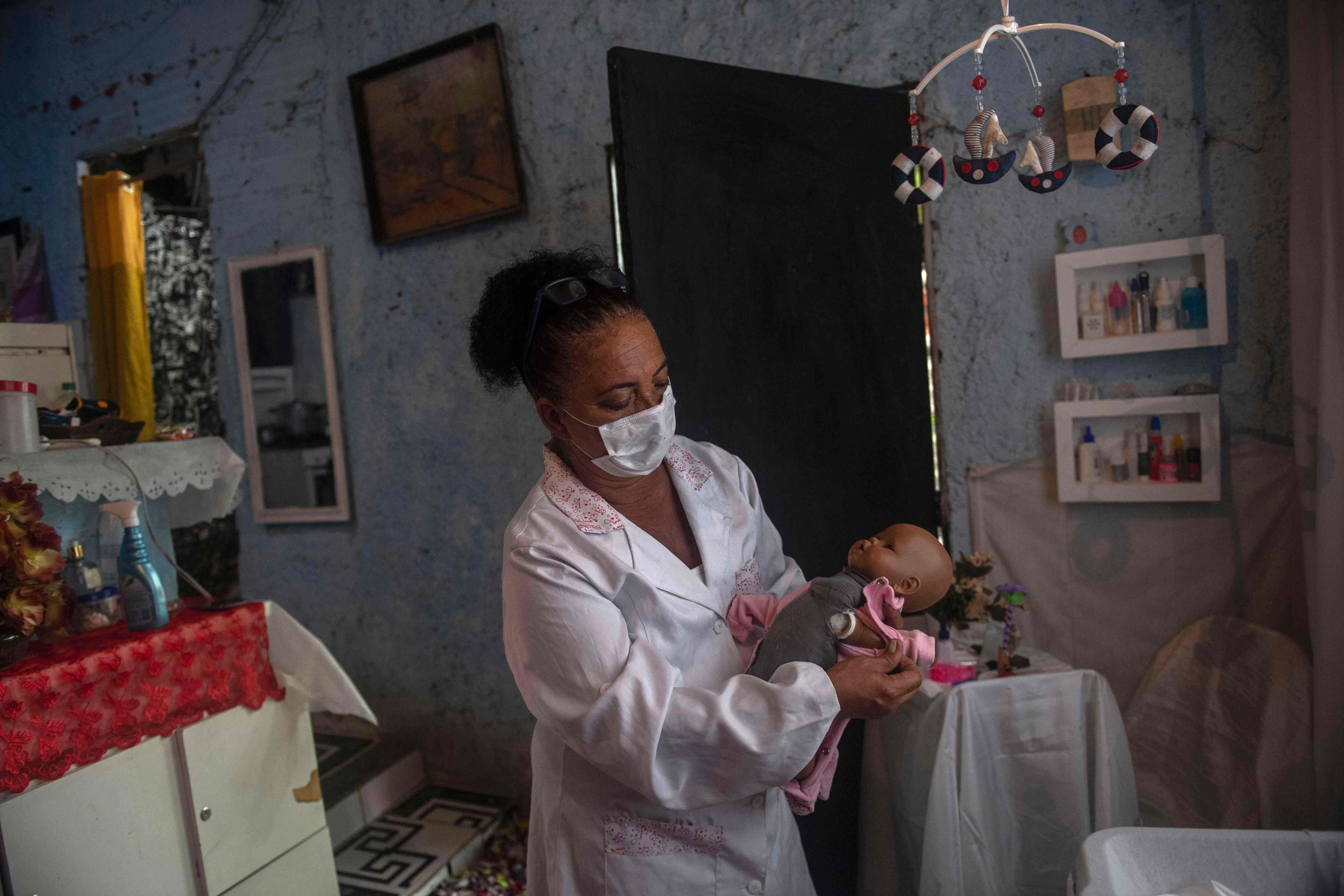 Suelen da Silva, quien perdió su trabajo en abril luego de la pandemia por el coronavirus, revisa una muñeca en el hospital que fundó en su casa en Niteroi, Río de Janeiro, Brasil. (Foto Prensa Libre: AFP)