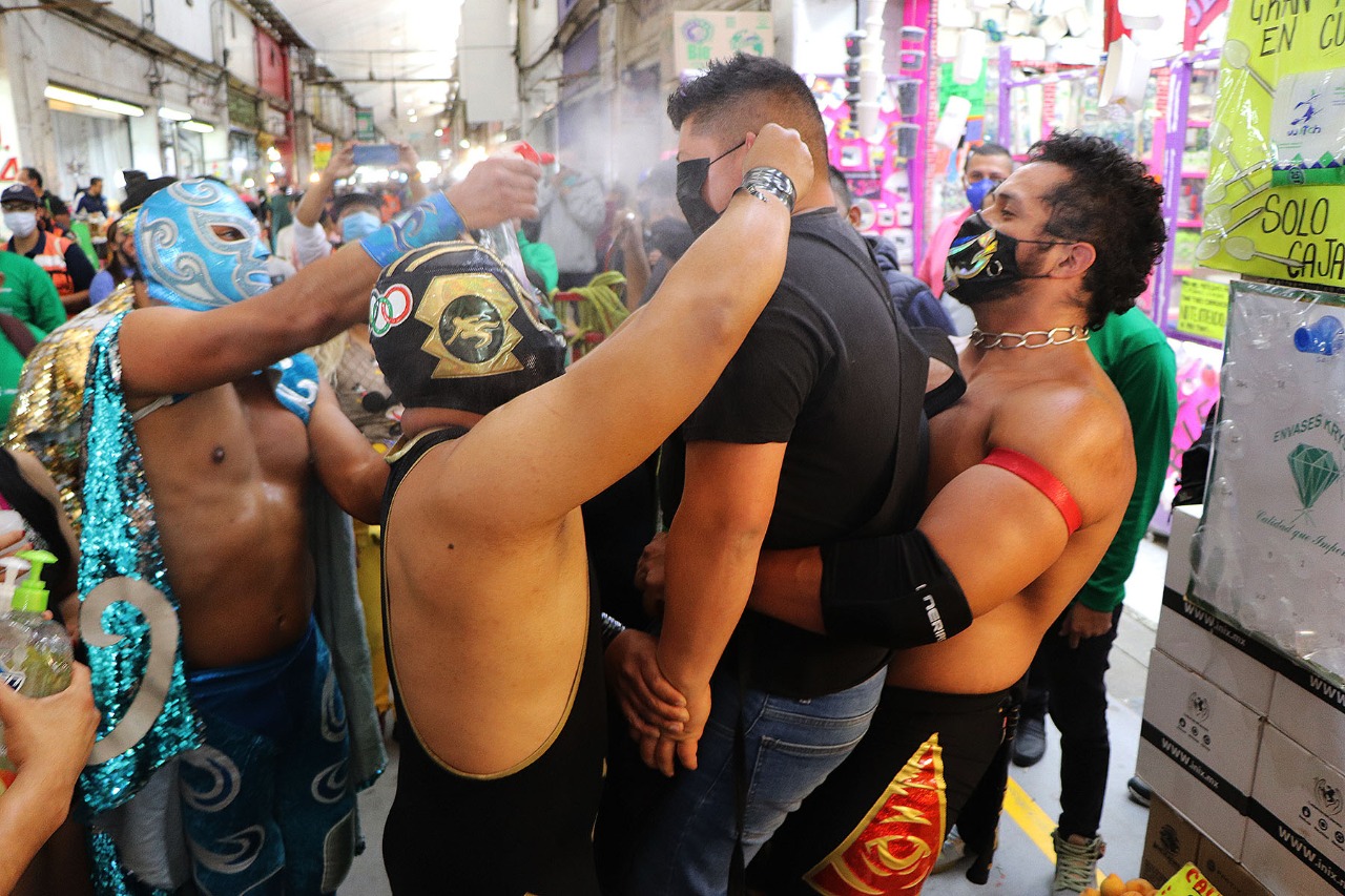 Los luchadores profesionales levantan a quienes no lleven mascarilla y los rocían con desinfectante. (Foto Prensa Libre: @CdeAbastoCDMX)