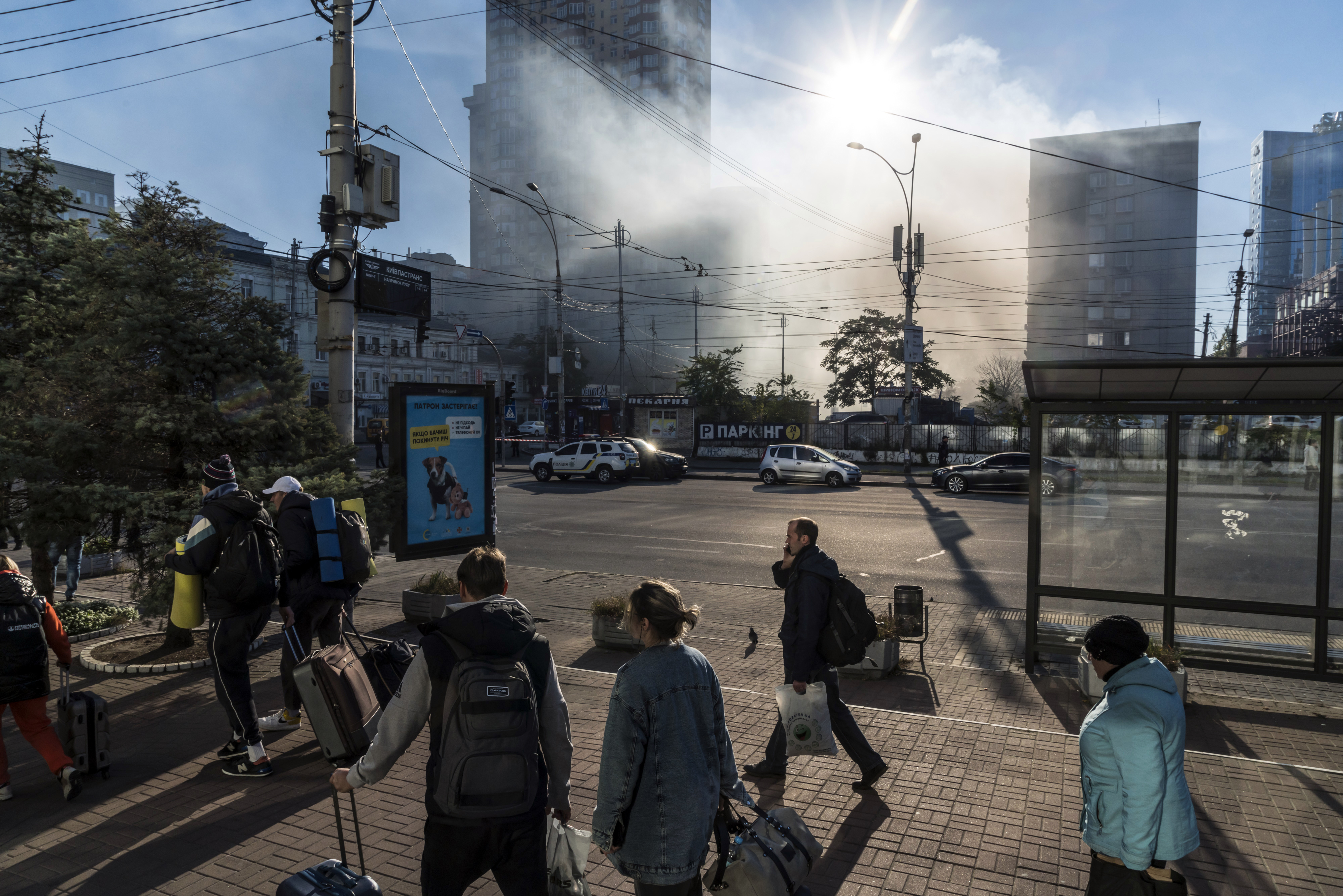 El humo sale del lugar de un ataque con drones mientras los pasajeros caminan con su equipaje desde las estaciones de tren y autobús cercanas en Kiev, Ucrania, el lunes 17 de octubre de 2022.  (Foto Prensa Libre: Brendan Hoffman/The New York Times)