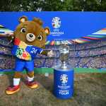 Albert, mascota de la Eurocopa 2024, posa junto a una maqueta del trofeo.