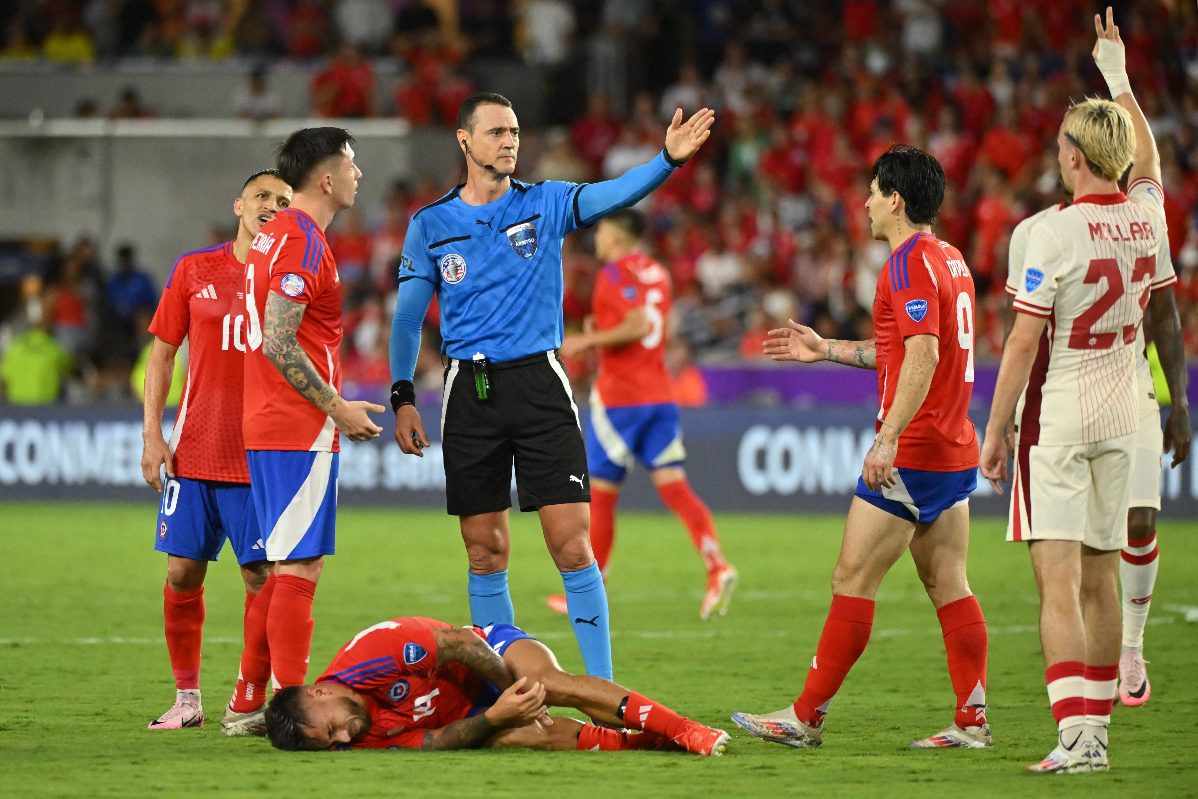 El árbitro, Wilmar Roldán, gesticula, mientras el chileno, Cristian Zavala, yace tirado en el terreno de juego durante el último partido del Grupo A, frente a Canadá. (Foto Prensa Libre: AFP)