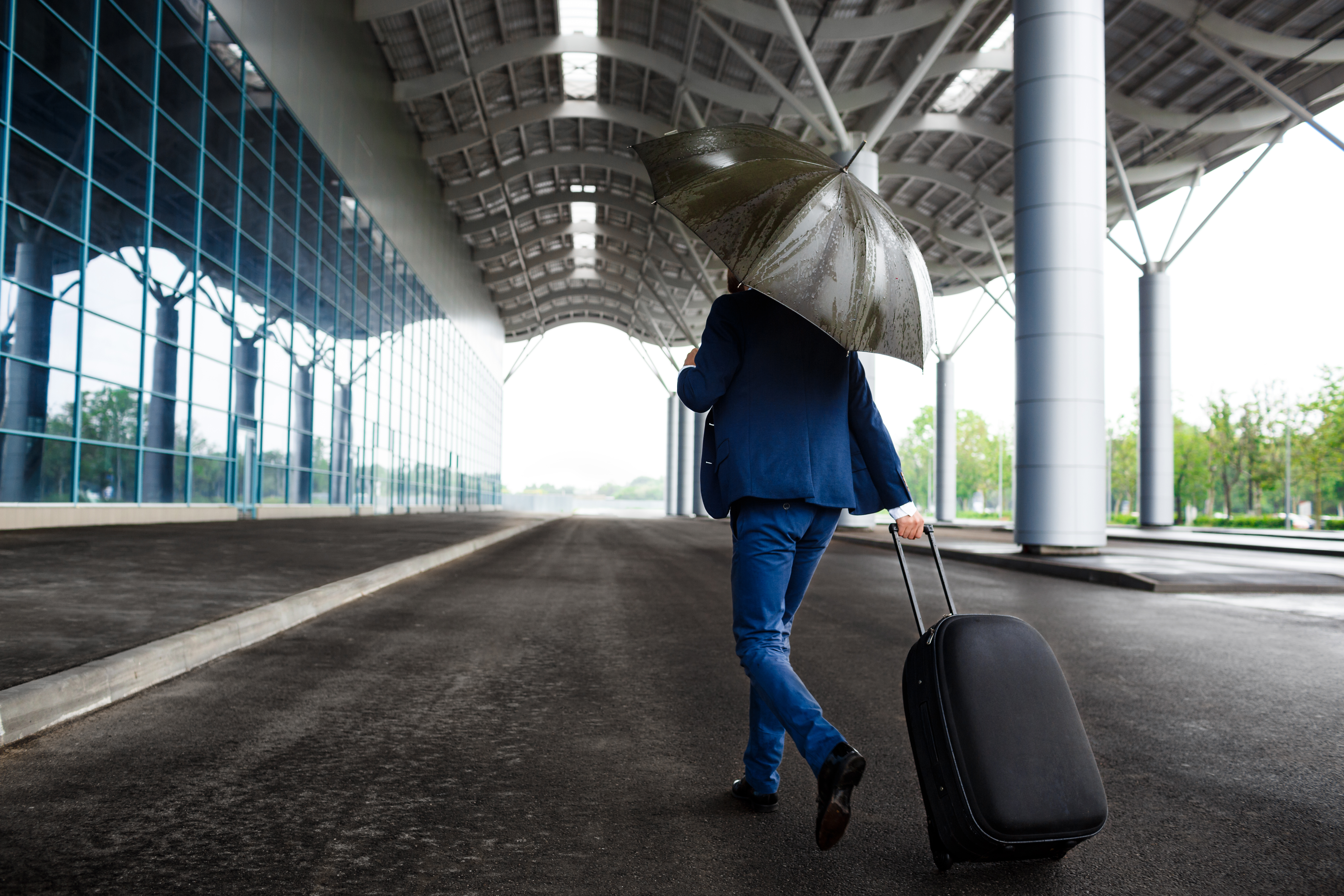 Picture of  young  businessman holding  suitcase and umbrella walking in rain