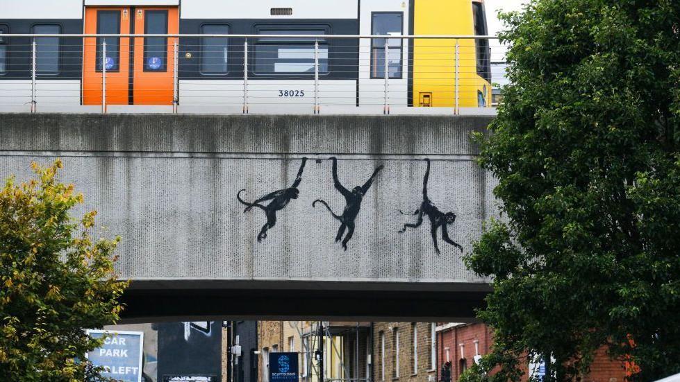 Pintura de tres monos colgando de un puente en Brick Lane