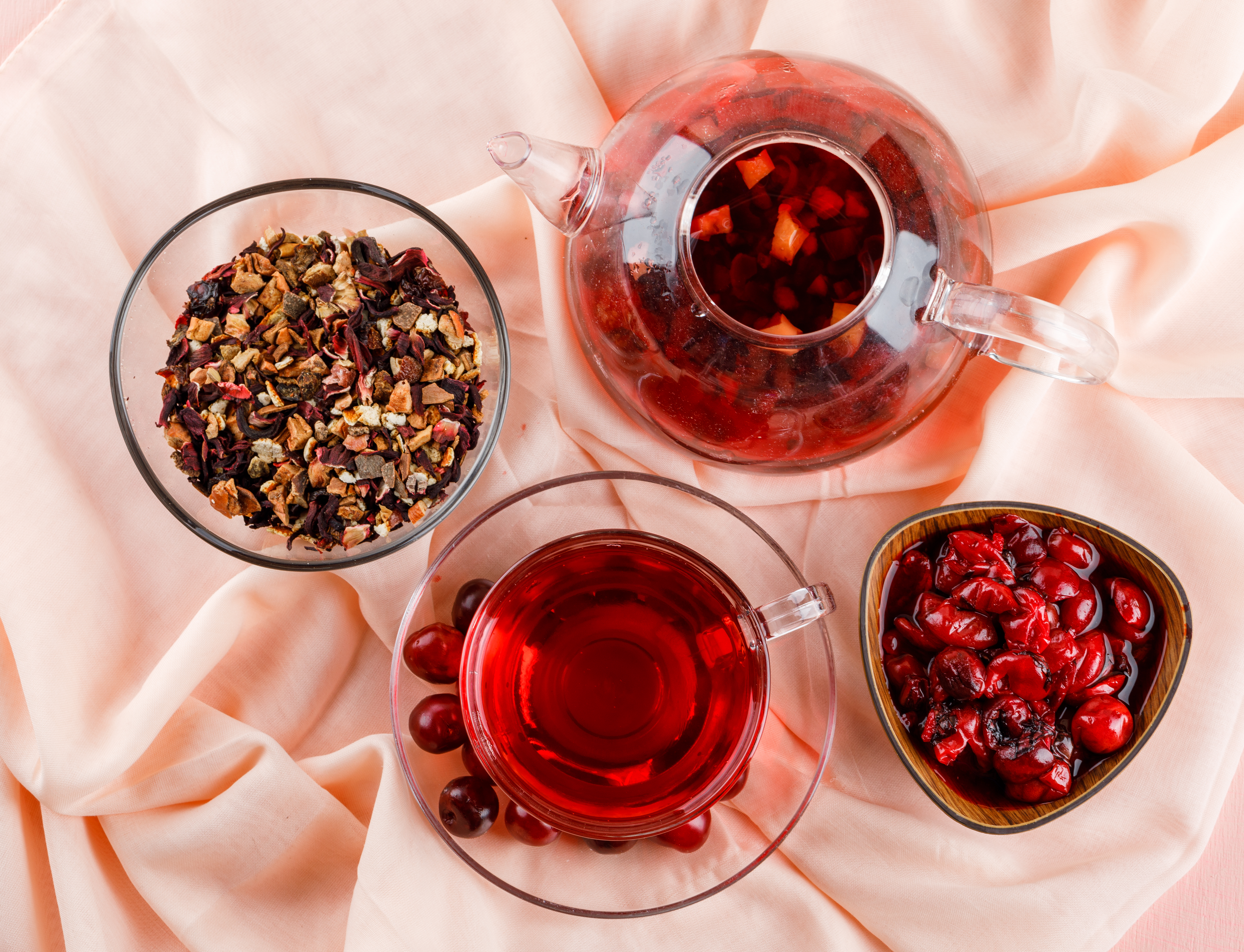 Cherry jam in a bowl with cherries, tea, dried herbs flat lay on pink and textile background