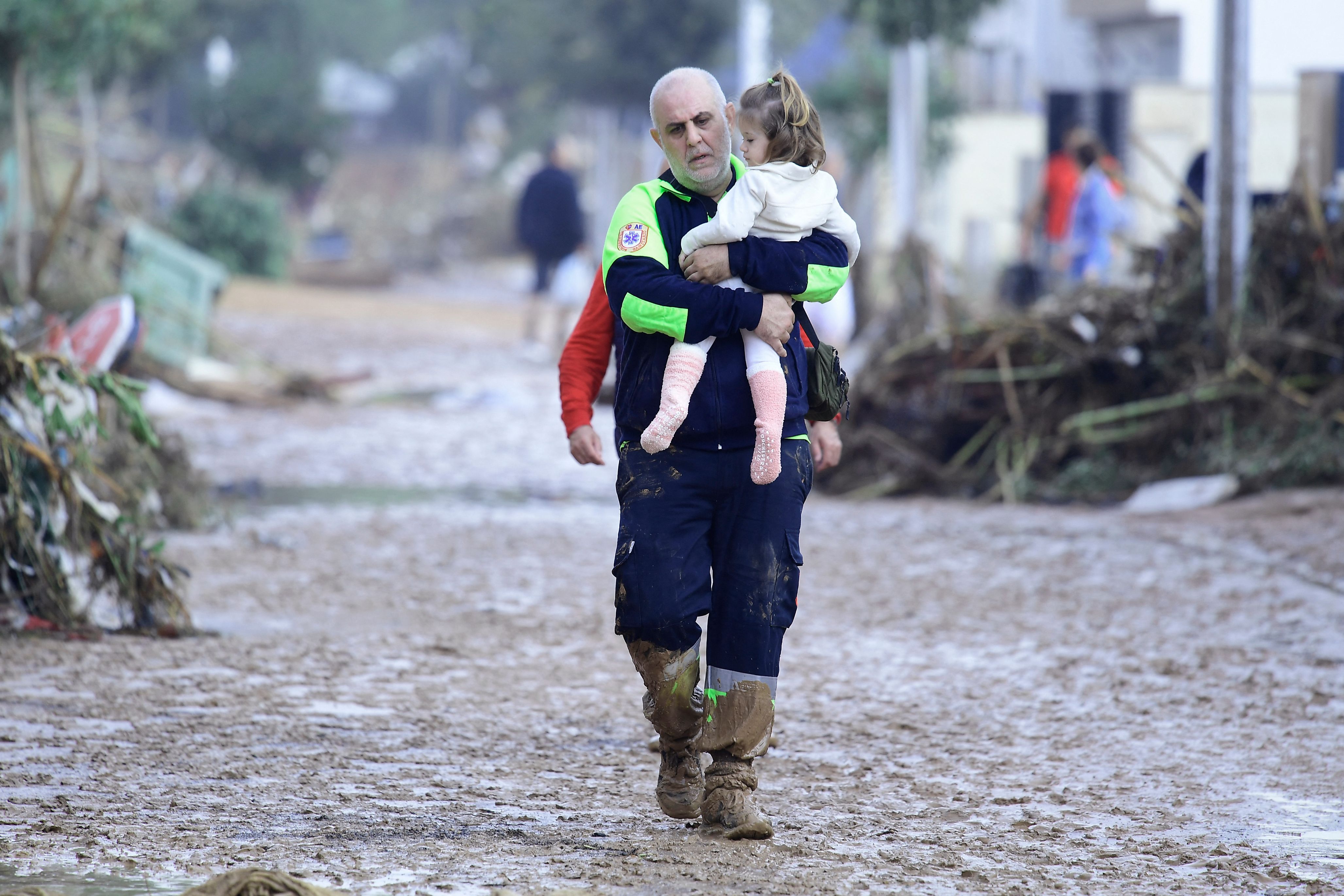 Un miembro de Protección Civil lleva a un niño por una calle cubierta de barro en una zona inundada en Picanya, cerca de Valencia.