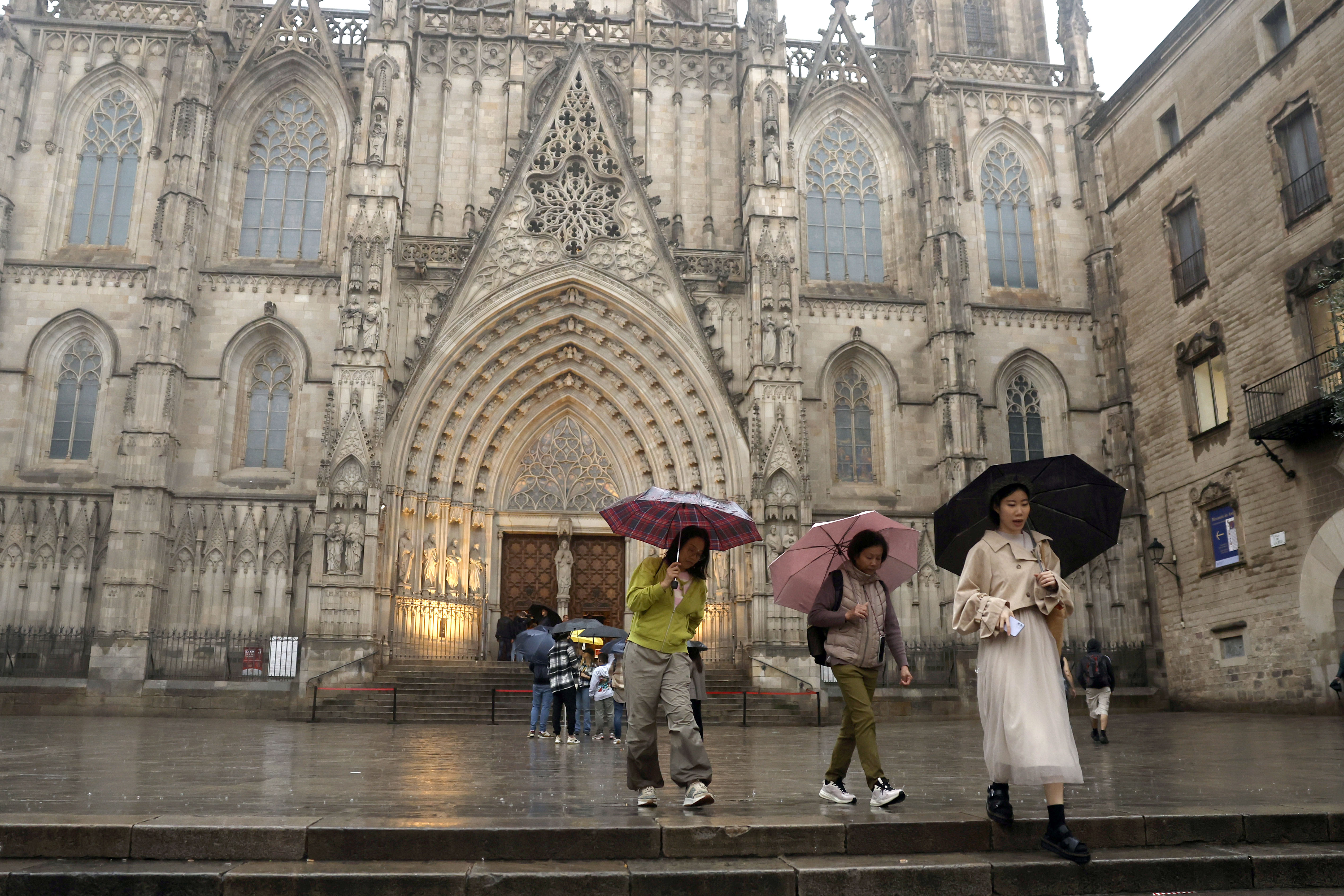 Varias personas se protegen de la lluvia ante la Catedral de Barcelona este lunes mientras autoridades están en alerta roja.  (Foto Prensa Libre: EFE/Toni Albir)