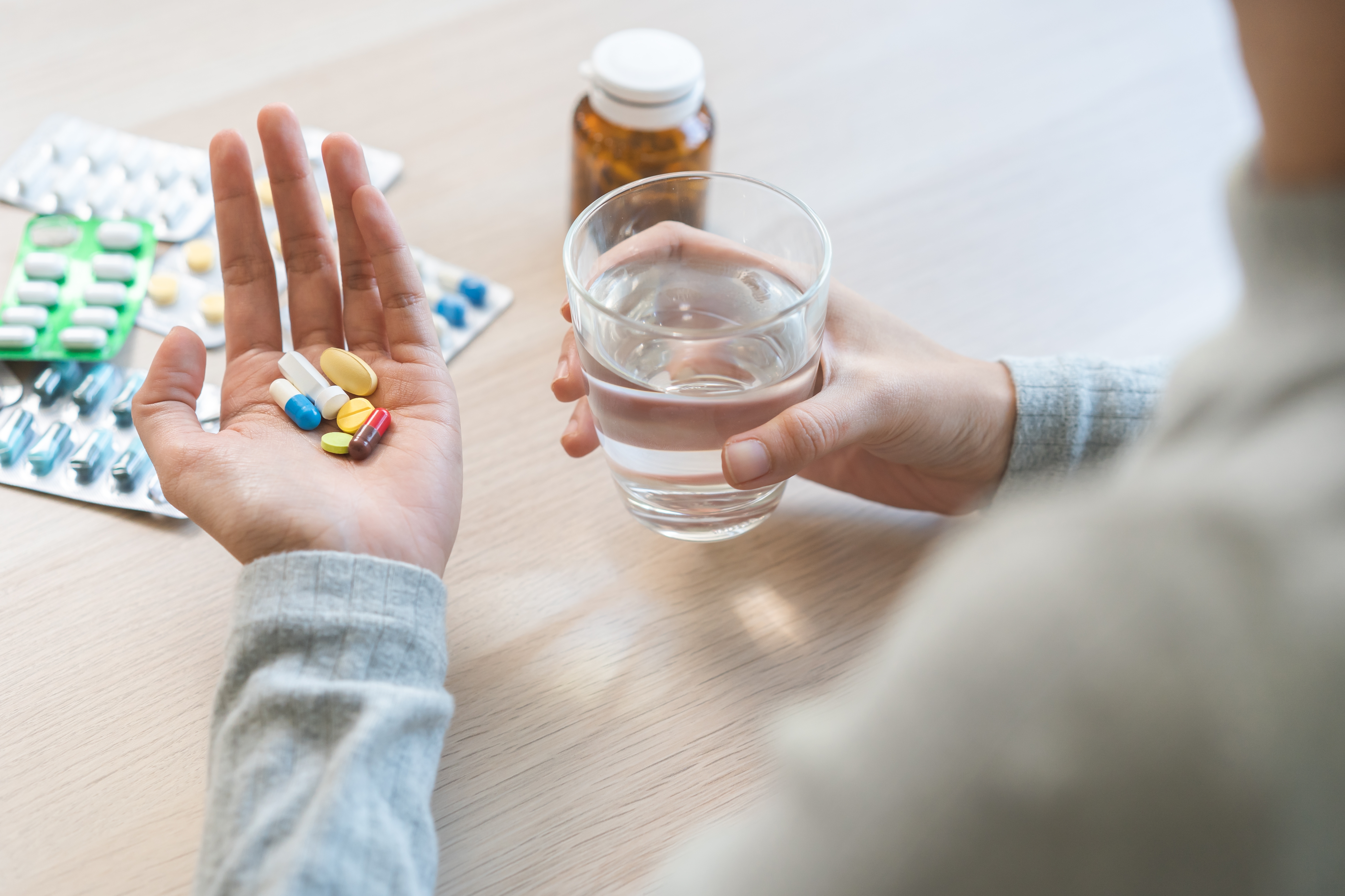 Cuidado de la salud de la enfermedad, la enfermedad de la mujer joven asiática, la mano de la muchacha que sostiene, toma la cápsula de las píldoras, medicina del analgésico para la gripe, dolor de cabeza para el tratamiento, toma la droga o la vitamina con un vaso de agua en casa.