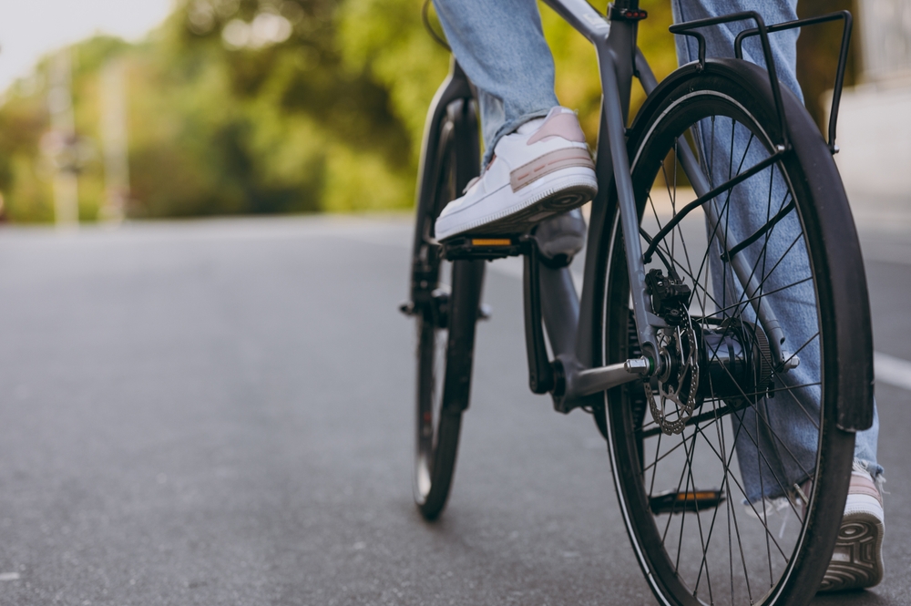 Foto recortada de una mujer joven con pantalones de mezclilla zapatillas de deporte blancas montando bicicleta en la carretera