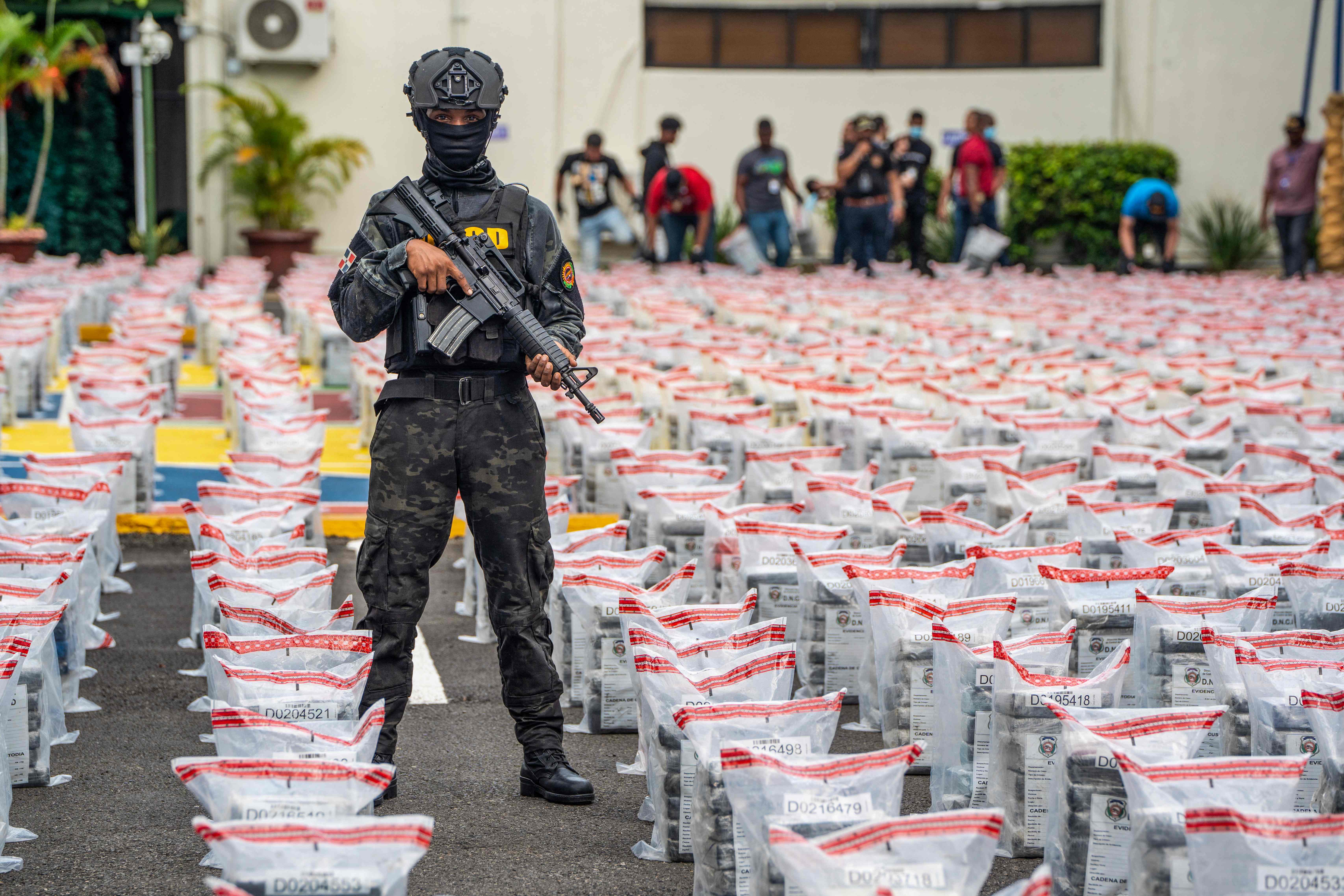 A member of the anti-drug corps stands guard next to the packages of suspected drugs at the National Drug Control Directorate (DNCD) after a seizure of 9.5 tonnes of suspected cocaine in Santo Domingo on December 6, 2024. Authorities in the Dominican Republic on Friday reported the seizure of 9.5 tonnes of suspected cocaine, the largest in its history. The seizure was made during an operation at the Caucedo Multimodal Port of Boca Chica, near the capital, Santo Domingo. The drugs were found in two containers of bananas from Guatemala destined for Belgium. (Photo by Francesco SPOTORNO / AFP)