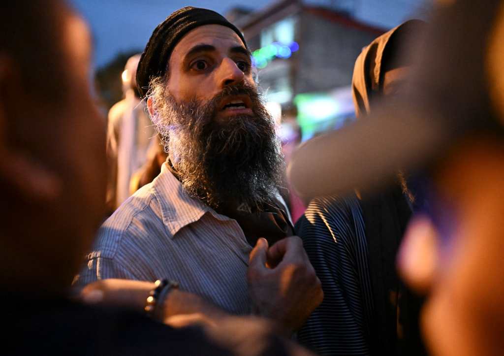 A member of the Lev Tahor Jewish community protests next to Guatemalan police members surrounding a minibus transferring some of the children rescued from the Jewish Lev Tahor sect to the Alida Espana de Arana special education school in Guatemala City on December 22, 2024. Relatives of the 160 children who were rescued from the ultra-Orthodox Jewish Lev Tahor sect, under investigation for alleged sexual abuse of minors, gathered outside a shelter in the capital to demand that the authorities return them. (Photo by Johan ORDÓÑEZ / AFP)