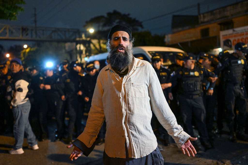 A member of the Lev Tahor Jewish community protests as Guatemalan police members surround a minibus transferring some of the rescued children to the Alida Espana de Arana special education school in Guatemala City on December 22, 2024. Guatemalan authorities on Friday rescued 160 children from a farm belonging to the Lev Tahor sect, an ultra-Orthodox Jewish group under investigation for alleged sexual abuse of minors, the Interior Minister and the Attorney General's Office announced. (Photo by Johan ORDÓÑEZ / AFP)