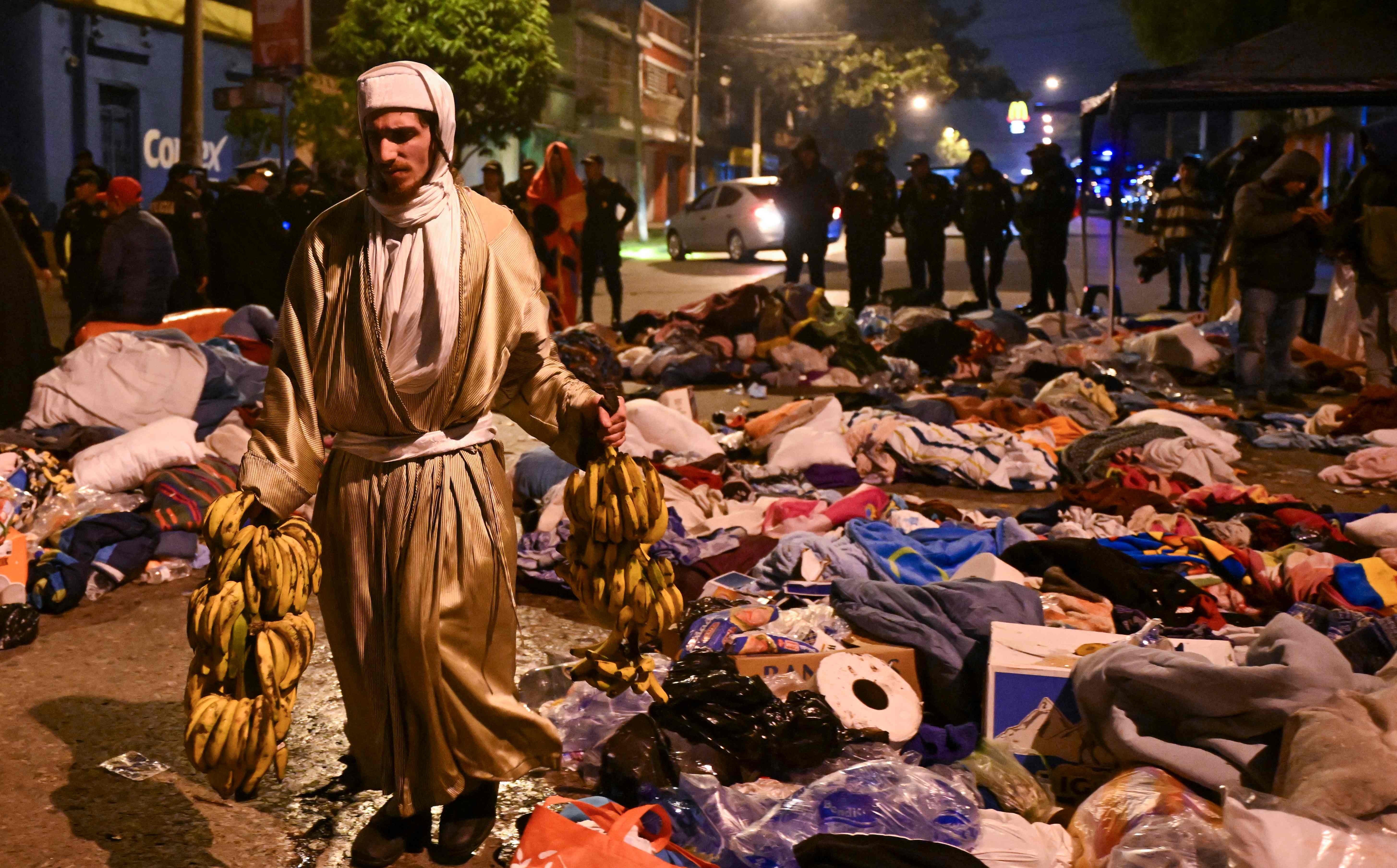 A man walks past the belongings of family members and some of the children who were rescued from the Lev Tahor Jewish sect and taken to a shelter following their recapture by police after attempting to leave the facility in Guatemala City on December 23, 2024. Relatives of the 160 children who were rescued from the ultra-Orthodox Jewish Lev Tahor sect, under investigation for alleged sexual abuse of minors, gathered outside a shelter in the capital to demand that the authorities return them. The family members, who belong to the sect, stood on a street in front of the headquarters of the Alida Espana Special Care Center for Children, where the children were taken. According to the Attorney General's Office (PGN), the members of the sect "broke into" the center where the minors were being held, "taking away" several of them, but with the help of the police, they "managed to locate and return all of them to safety." (Photo by JOHAN ORDONEZ / AFP)