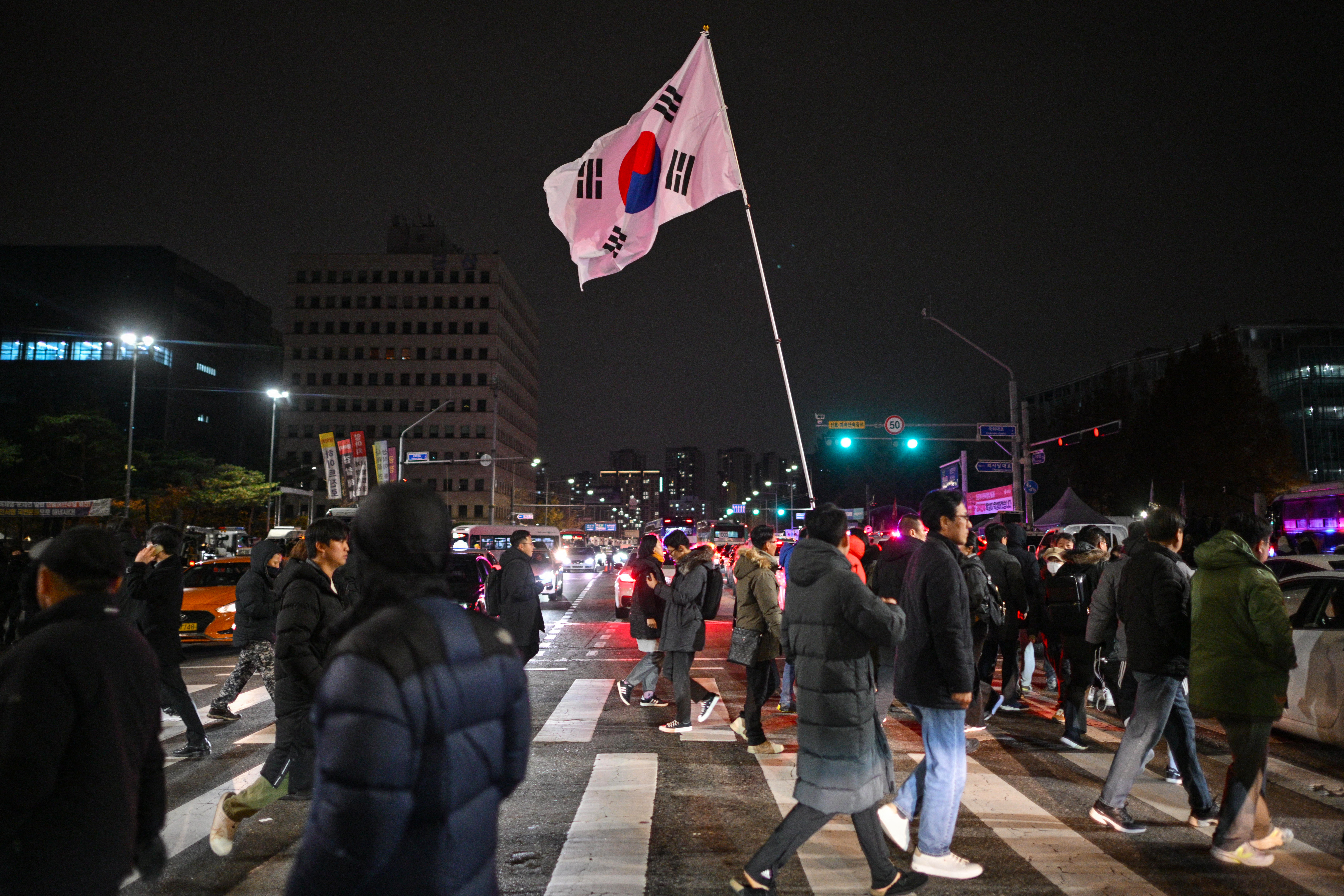 A man holds the South Korea flag outside the National Assembly in Seoul on December 4, 2024, after President Yoon Suk Yeol declared emergency martial law. - South Korea's President Yoon Suk Yeol on December 3 declared emergency martial law, saying the step was necessary to protect the country from "communist forces" amid parliamentary wrangling over a budget bill. (Photo by ANTHONY WALLACE / AFP)