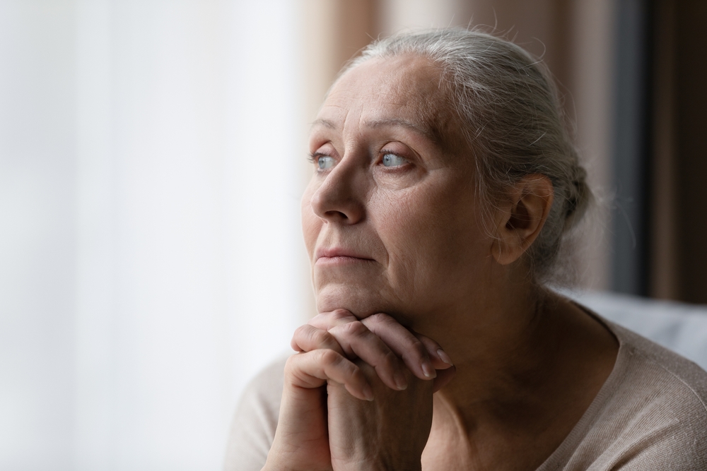 Una mujer aburrida de 70 años que mira por la ventana, se siente deprimida, frustrada, solitaria, sufre de pérdida de memoria, demencia, enfermedad de Alzheimer, trastorno mental. Concepto de problemas de la vejez