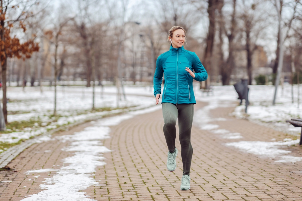 Encajar a una deportista corriendo por el camino en el parque en un día de invierno nevado. Recreación, clima de nieve, día de invierno