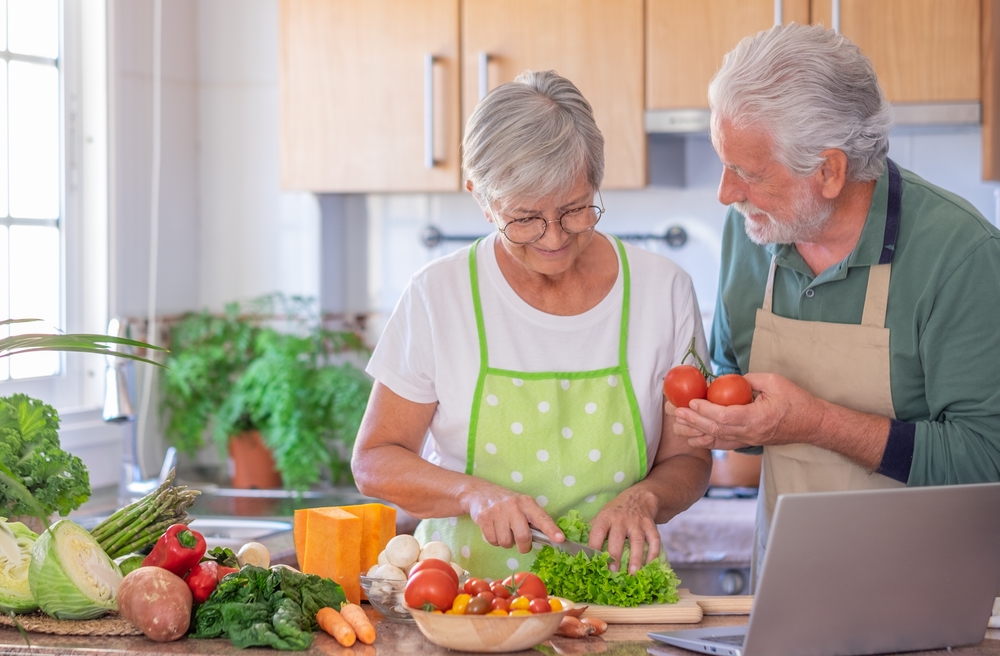 Atractiva pareja de ancianos sonrientes trabajando juntos en la cocina de casa preparando verduras disfrutando de una comida saludable.