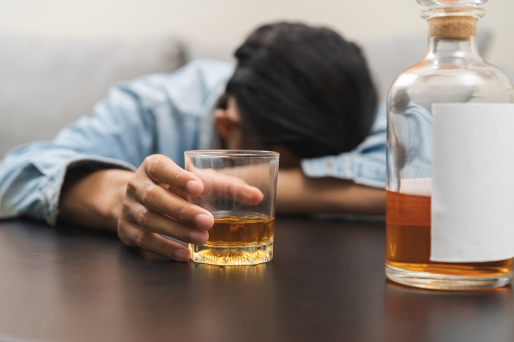 El alcoholismo del cuidado de la salud borracho, fatiga joven asiático sosteniendo un vaso de whisky, bebida masculina deprimida alcohol, dormir en la mesa en casa. Tratamiento de la adicción al alcohol, padece el problema de abuso alcoholismo.