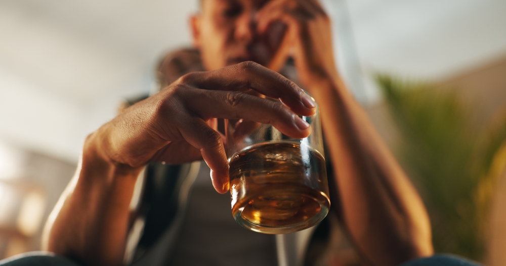 Alcohol, estrés y copa de whisky con una persona en la sala de estar por abuso de sustancias, riesgo y depresión. Salud mental, vino y licor con bebida en casa para la tentación, el retiro y el control