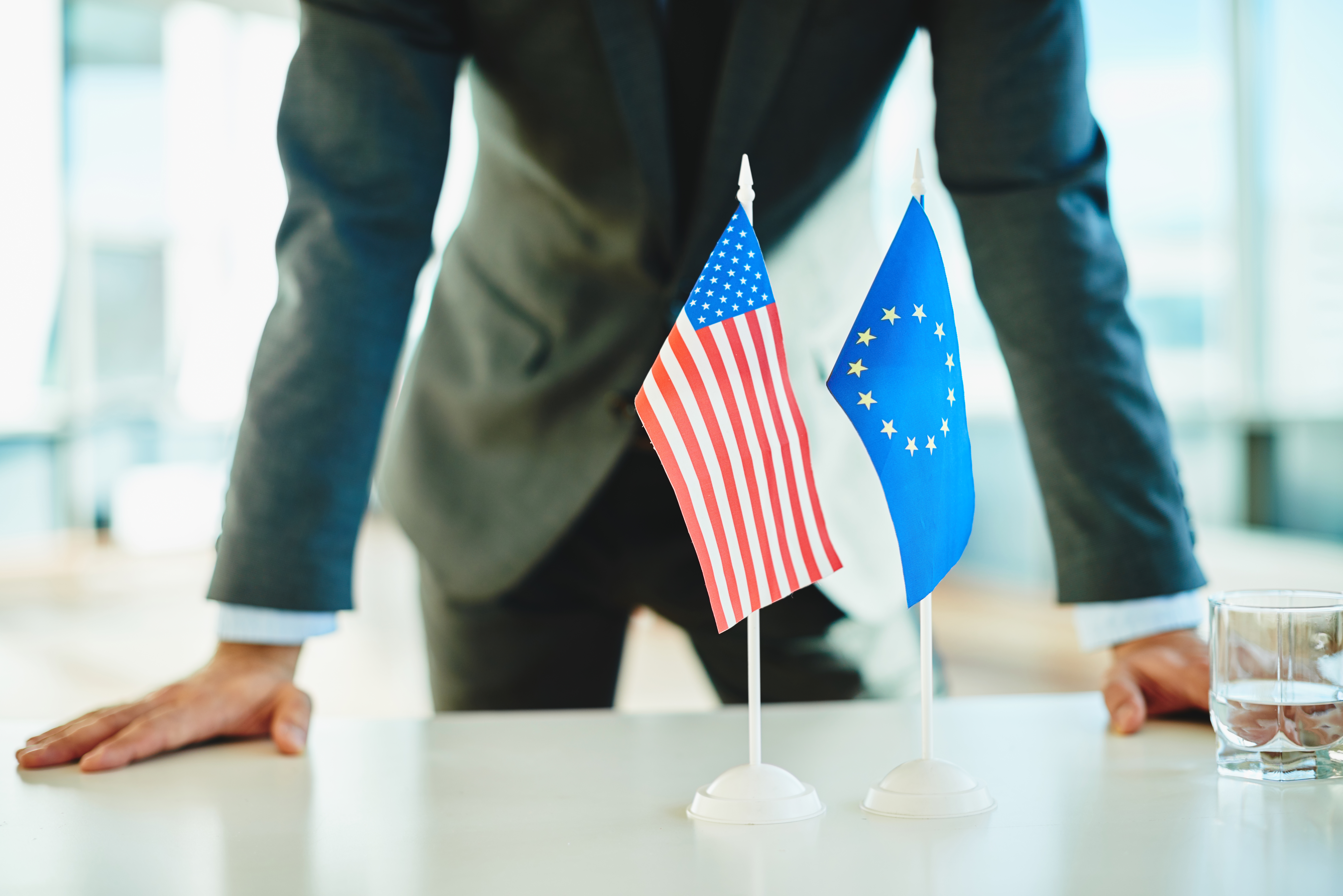 un hombre de negocios frente a una bandera de Estados Unidos y la Unión Europea