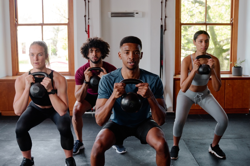 Grupo de adultos jóvenes focalizados haciendo campanarios de kétlebell en el gimnasio