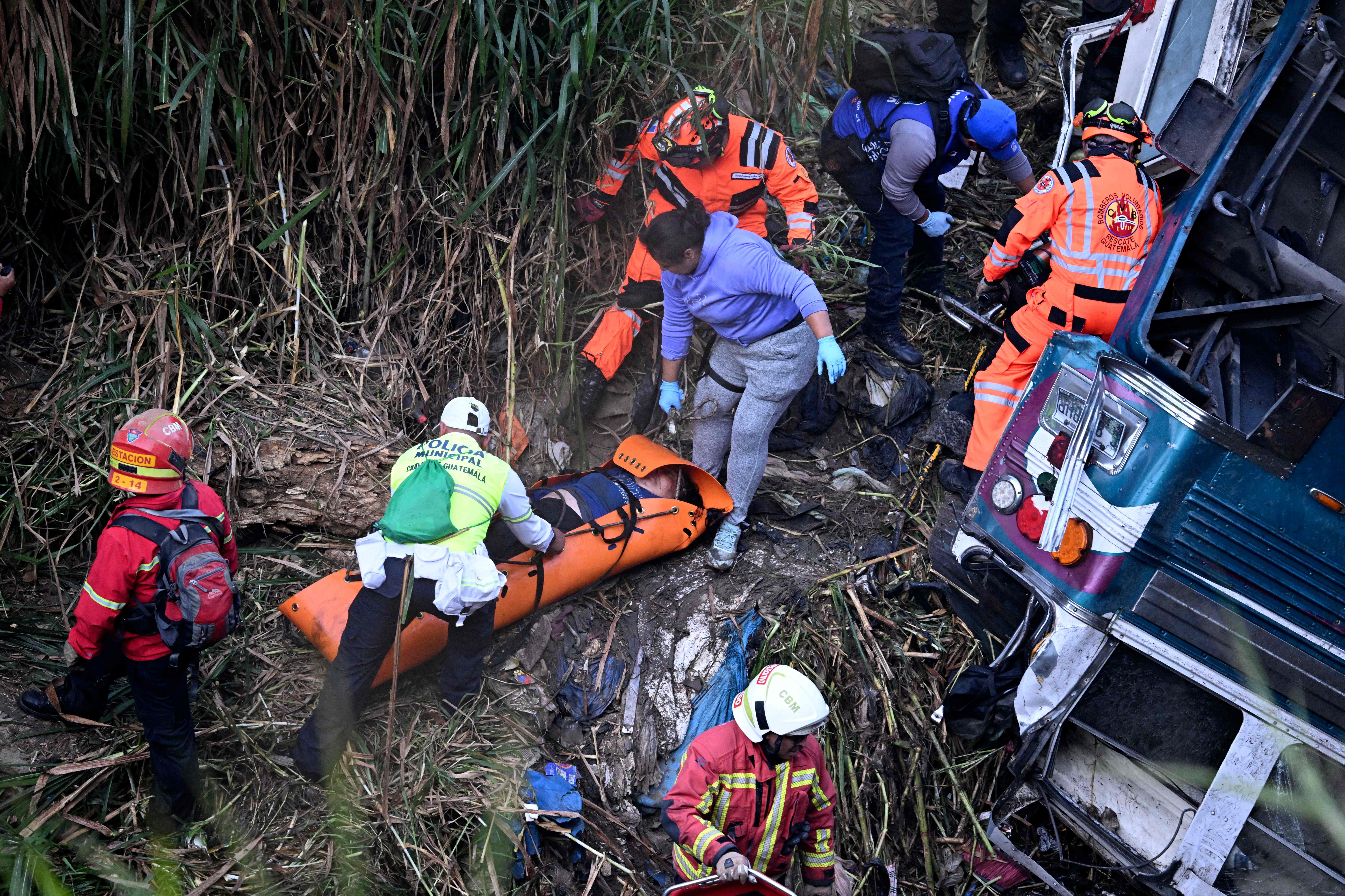 Firefighters and police work at the scene of an accident in which a bus fell down a ravine in Guatemala City on February 10, 2025. A bus carrying 75 people plunged into a ravine in Guatemala City on Monday, killing at least 31 people, rescue workers said. (Photo by Johan ORDONEZ / AFP)