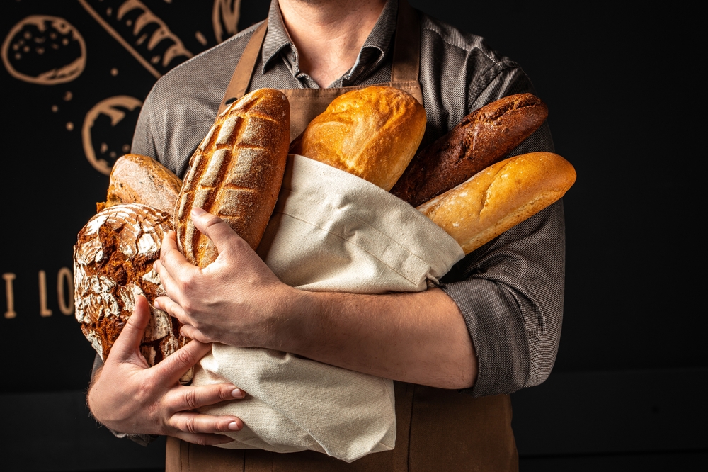 Man with different types of bread. Bakery products on dark background.