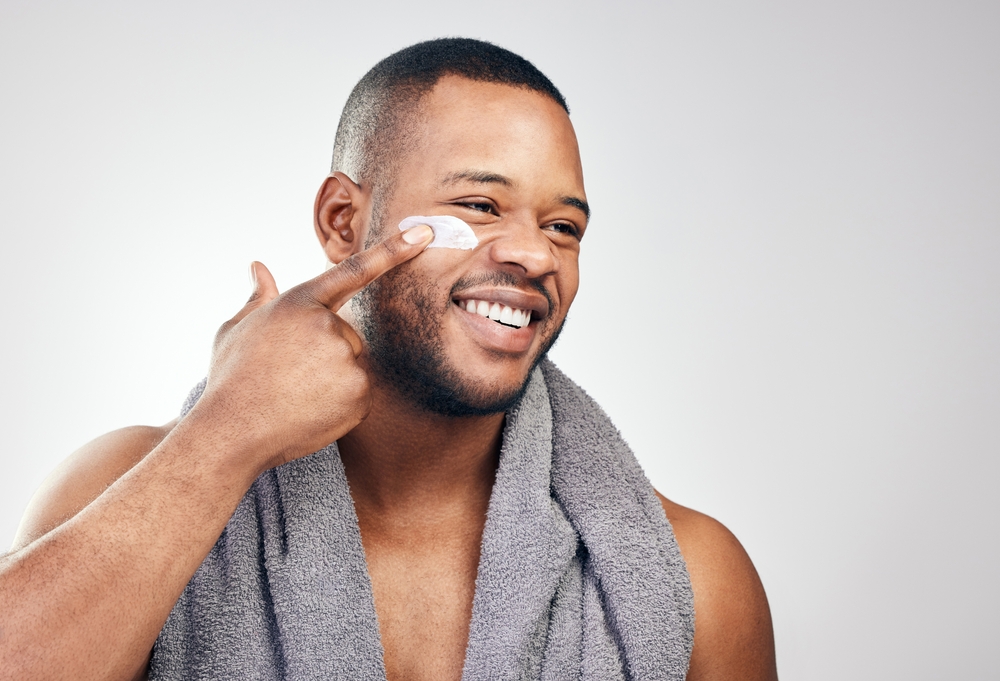 Black man, face cream and smile in studio for beauty with application, cosmetics and pride mockup.